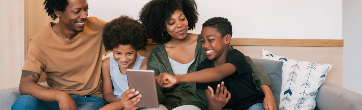 Família aparentemente felizes, sentados em um sofá mexendo em um tablet que está na mão da mãe